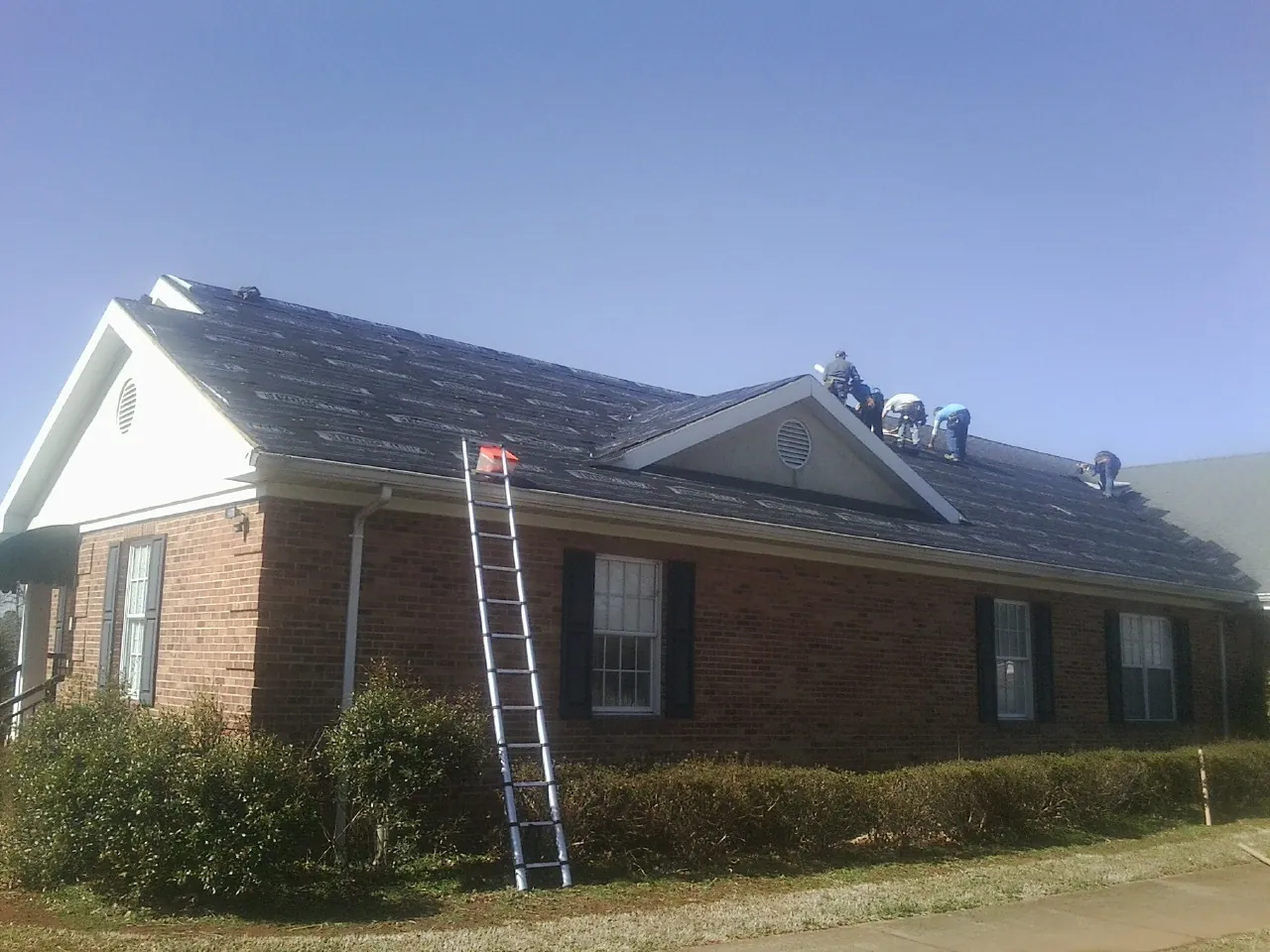 Crew tearing shingles off a brick ranch roof with a ladder set — Metal Roof Repair work by our crew in Chester