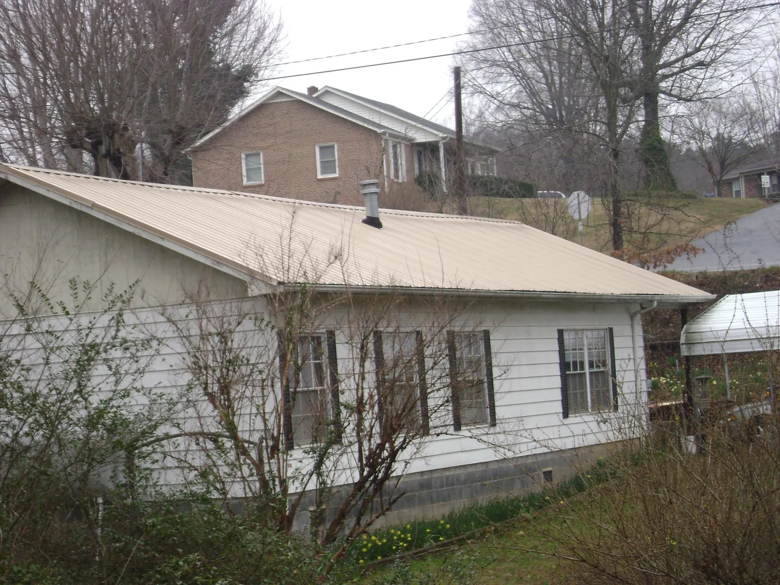 Tan metal roof on a white sided house set into a hillside — Commercial Roofing by Roofing Brothers in Chester